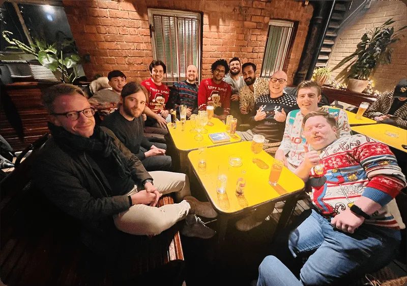The Kubicle team gathered around a yellow table at a Christmas dinner, smiling together.